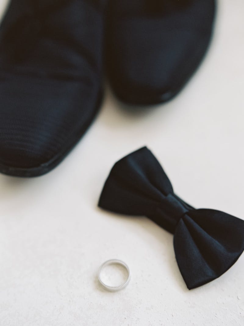 Groom attire wedding details with black bow tie, black loafers to go with a tuxedo, and silver wedding ring