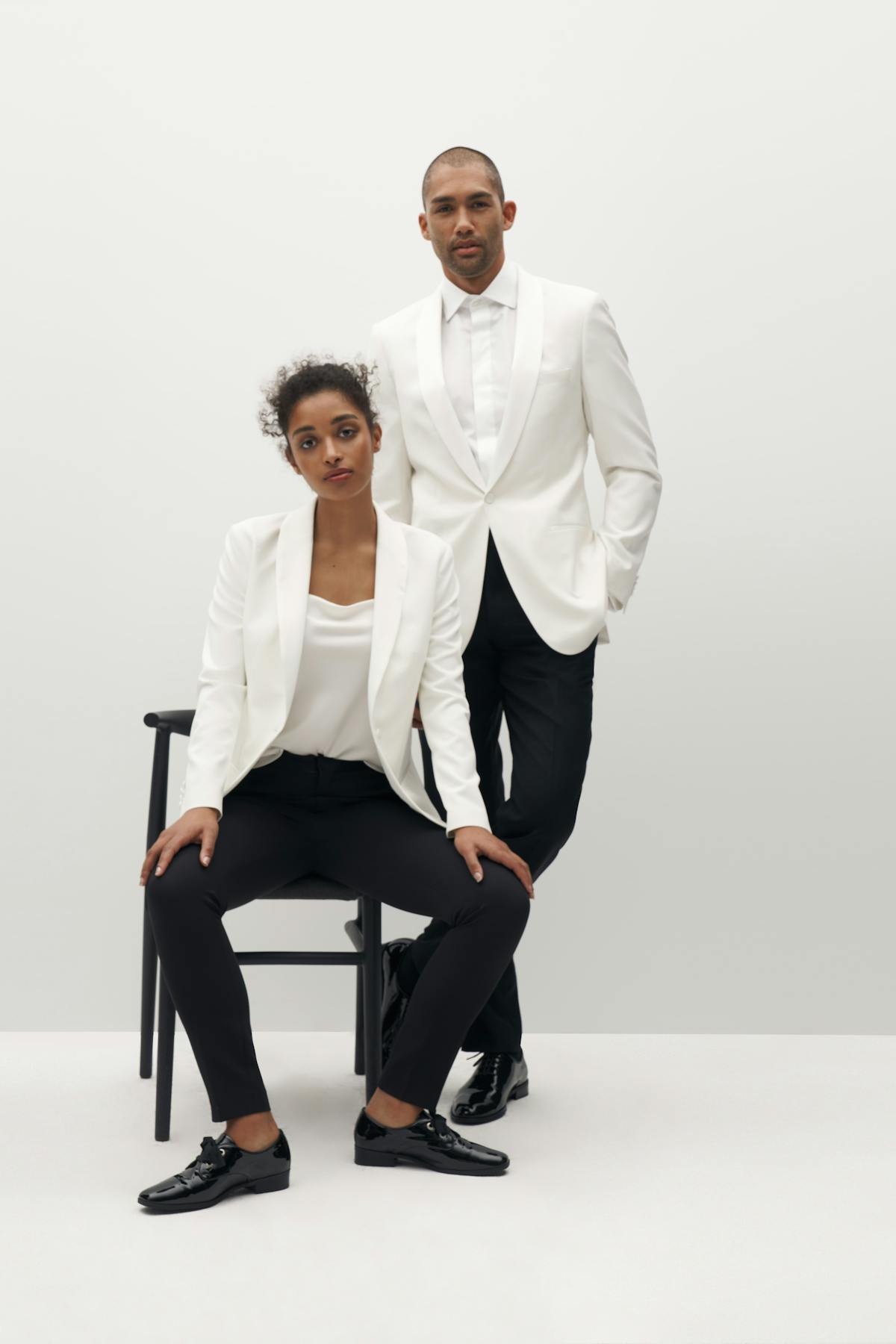 Man and woman posing in chair wearing white tuxedo jackets for a holiday gala.