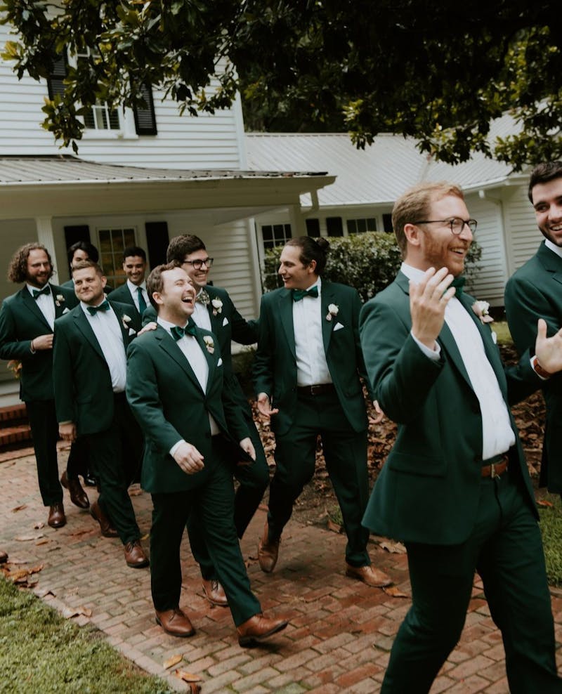 Groomsmen at backyard wedding in forest green suits and matching green bowties with brown shoes.