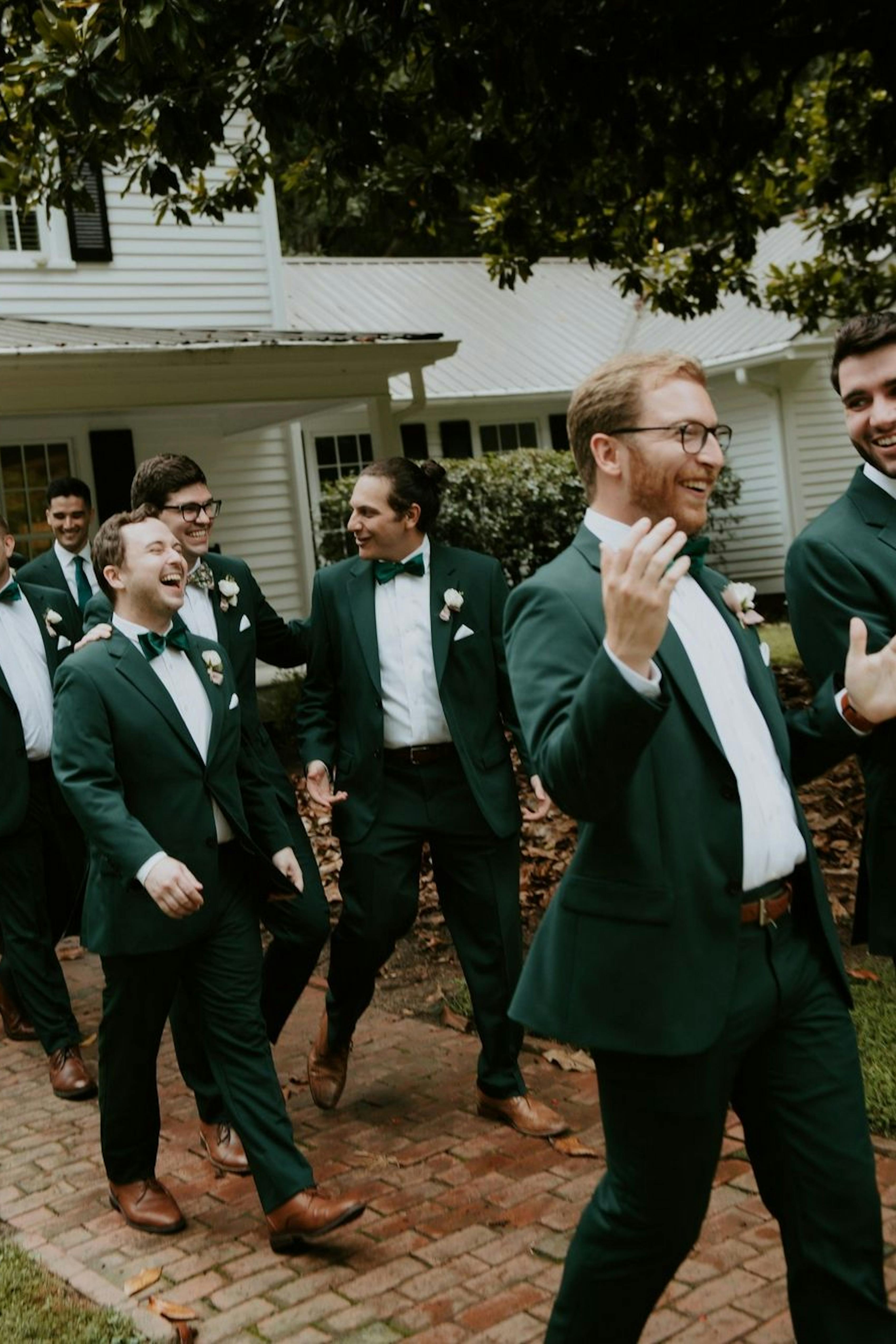 Groomsmen at backyard wedding in forest green suits and matching green bowties with brown shoes.