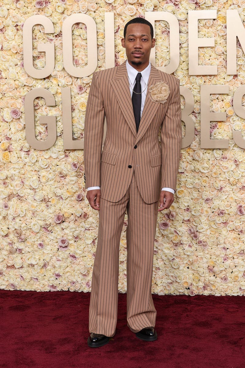 Tyler James Williams at the 2024 Golden Globes red carpet in tan pinstripe suit with fabric flower rosette at the lapel.