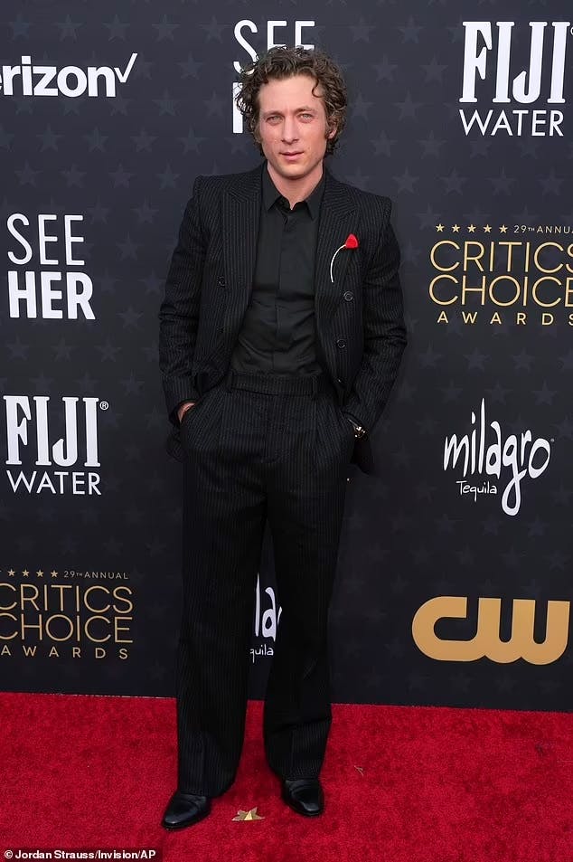Jeremy Allen White at the 2024 Critics Choice Awards red carpet in an all black outfit with a black pinstripe tuxedo and red rose lapel pin.