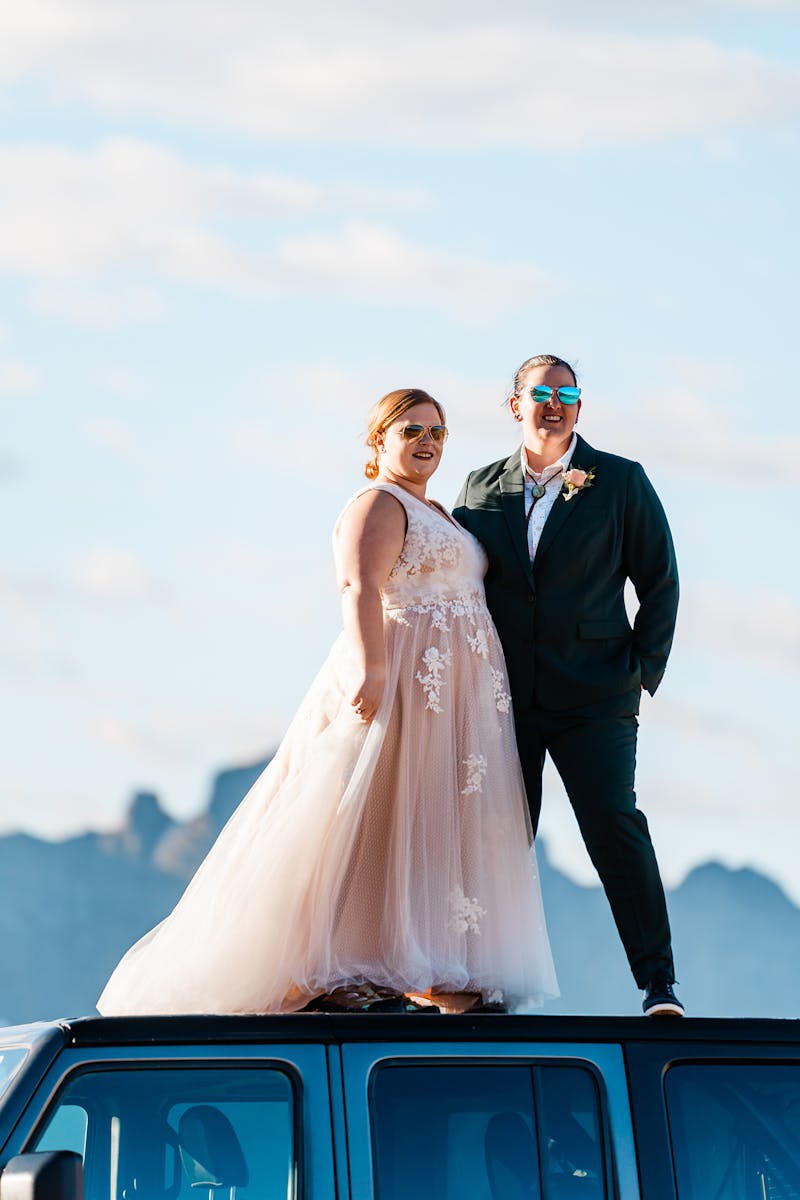 Lesbian brides celebrating in green wedding suit for women and blush ballgown.