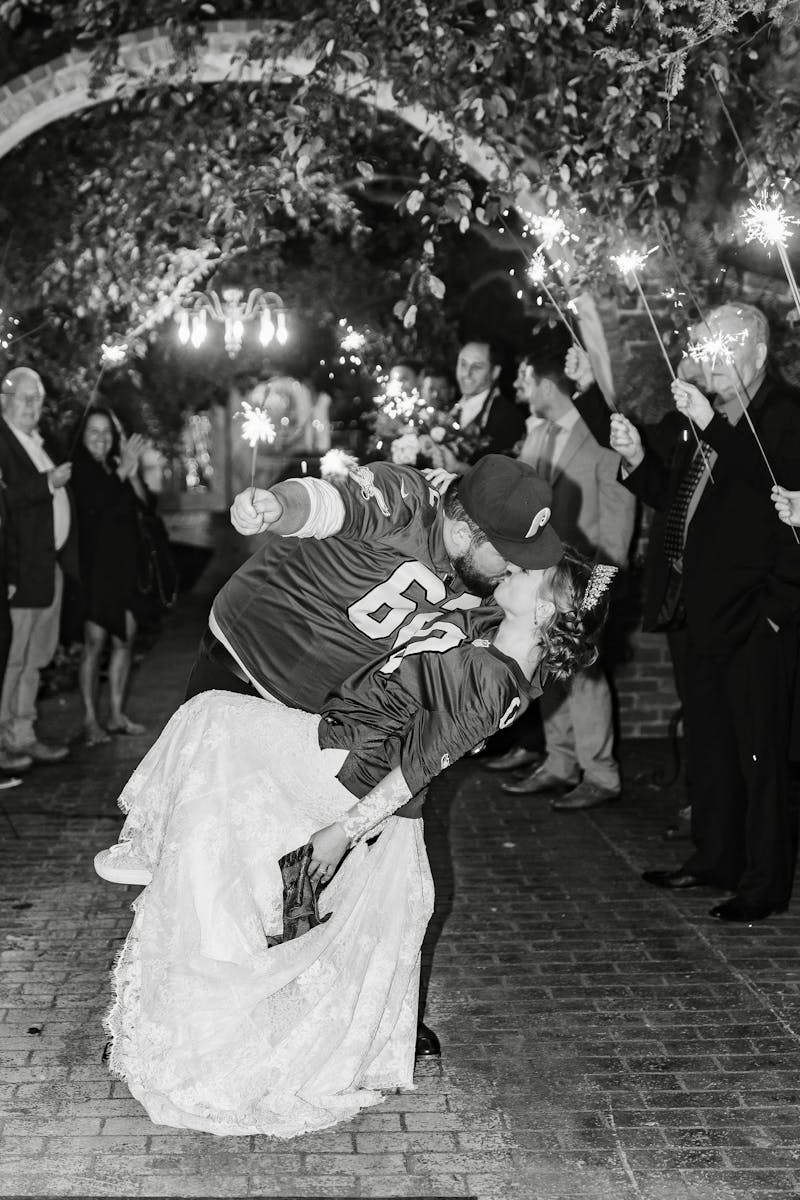 Sports themed wedding kiss under floral arch with sparkers.