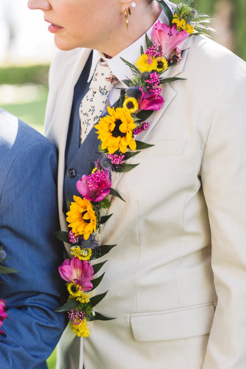 Women's tan suit for weddings with a light blue suit best, dainty floral tie, and lapel florals in bright colors