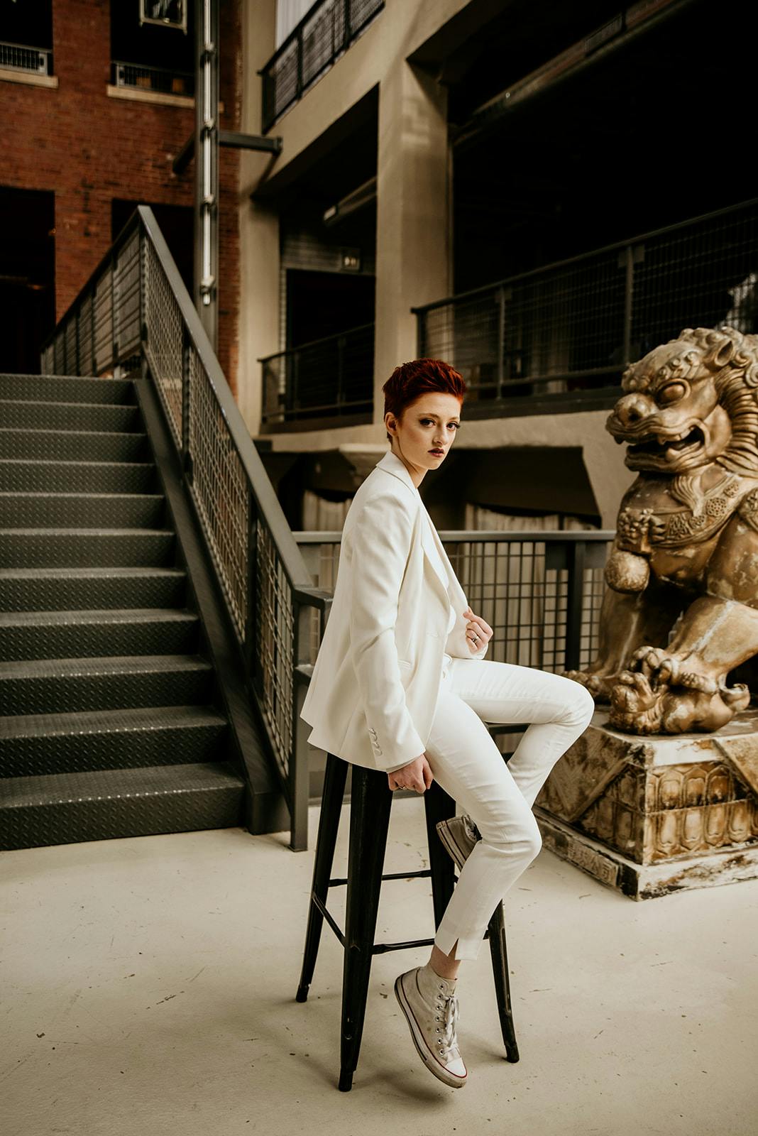 Androgynous woman in women's white tuxedo paired with white converse for a suit and sneakers casual look as a fashionable women's office outfit.