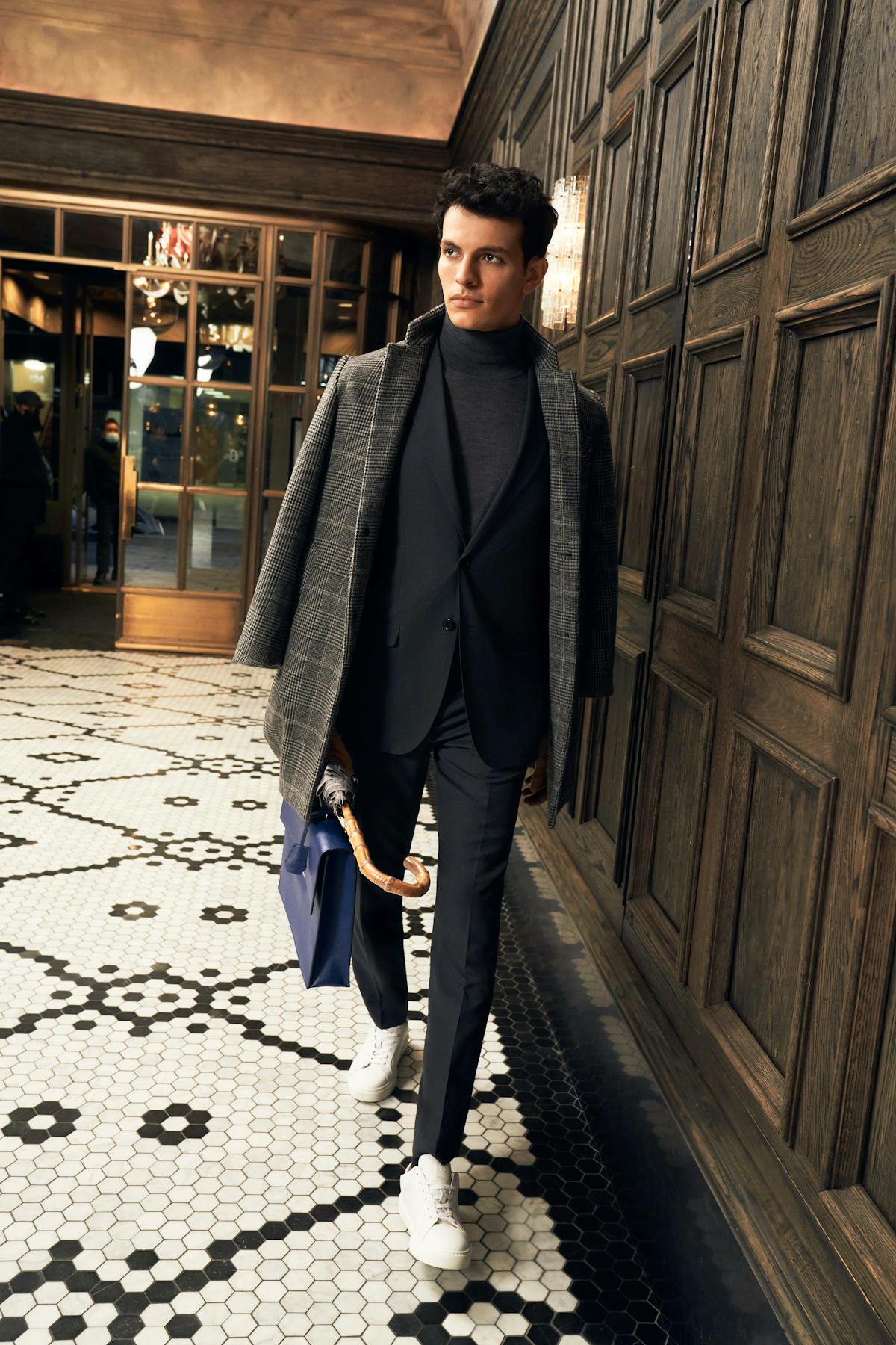 Layered suit workwear outfit with a dark grey men's suit, turtleneck, and overcoat for suits paired with a briefcase.