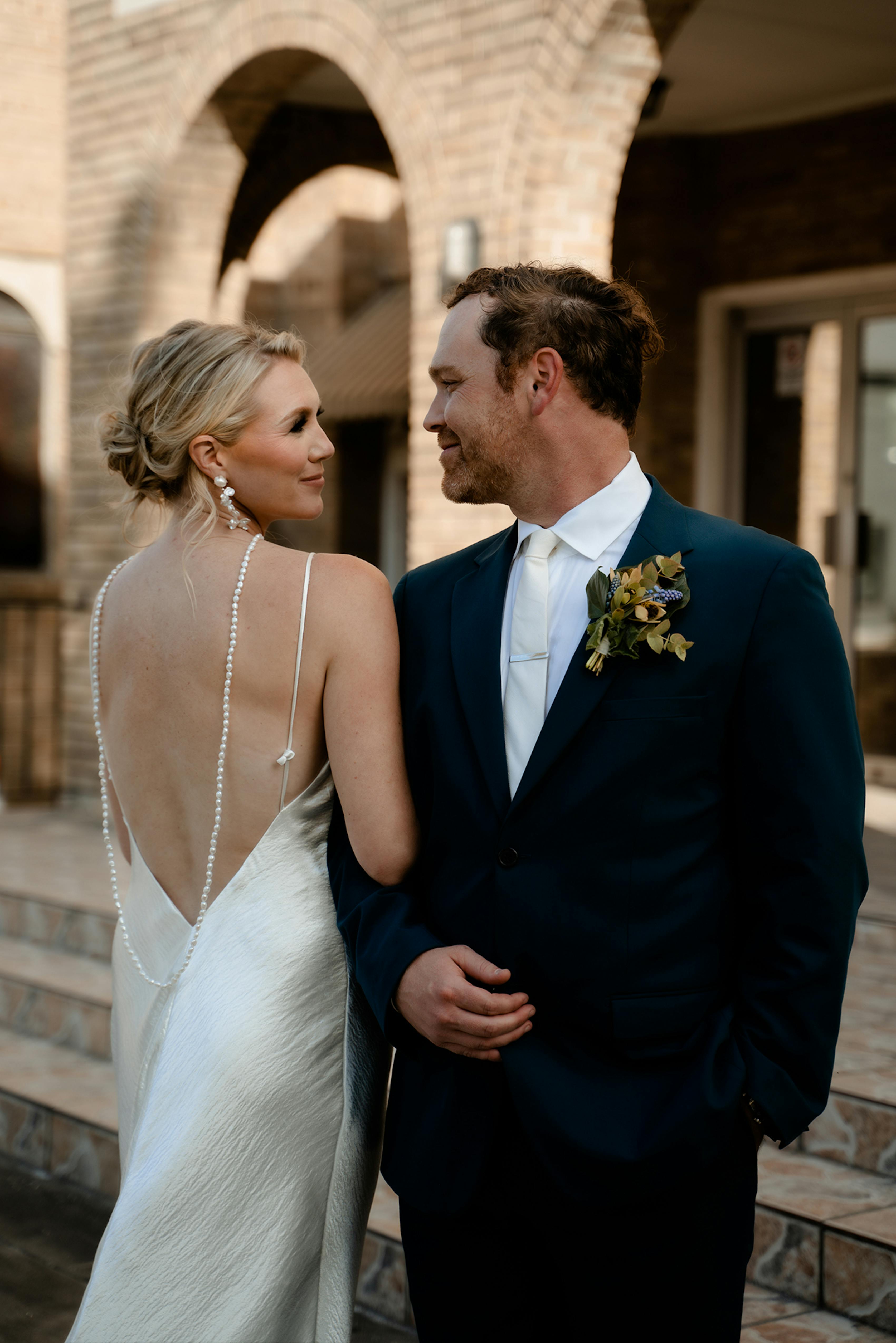 Bride in silky modern wedding dress and and groom in bold green suit.