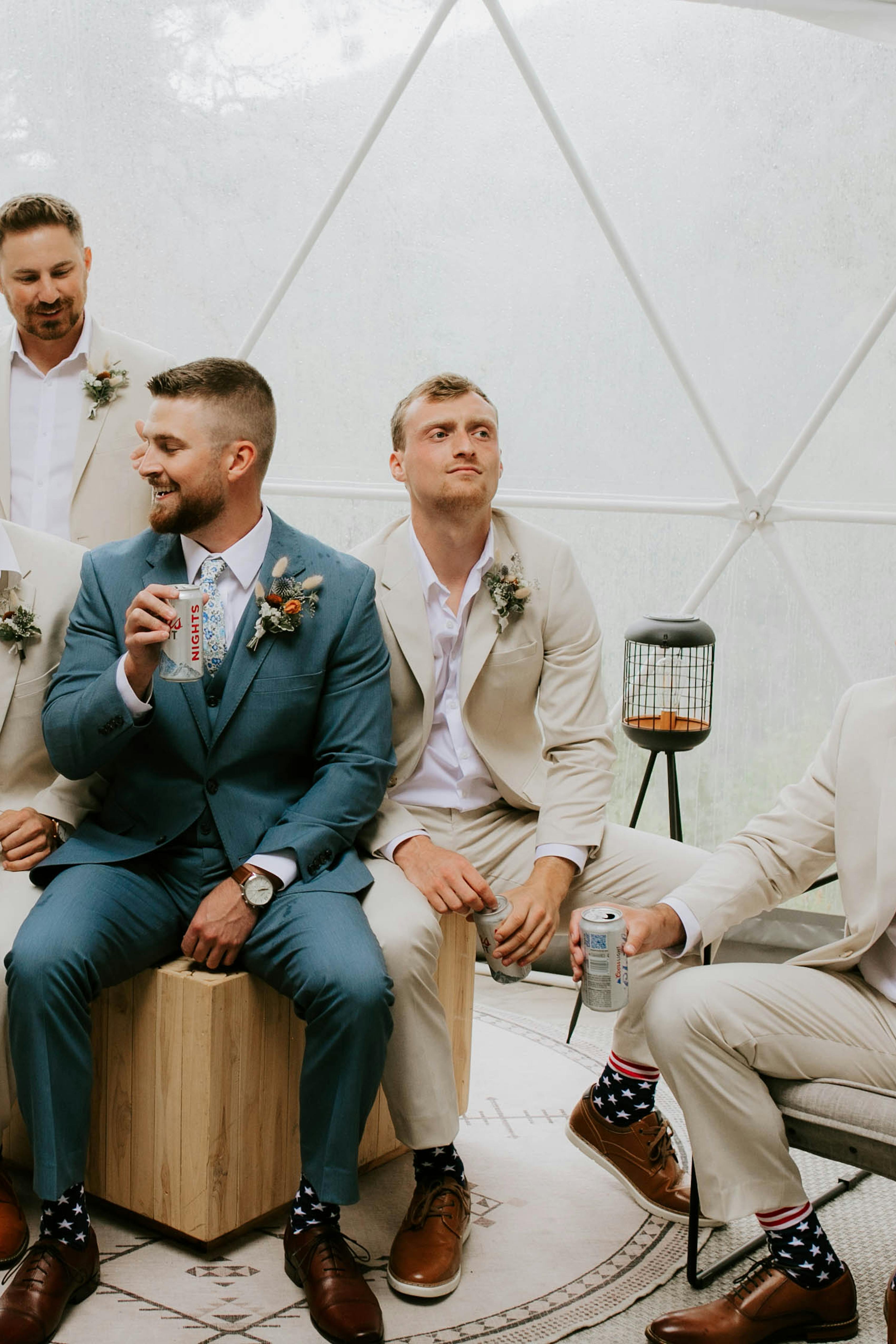 Outdoorsy groomsmen group drinking beer in tan groomsmen suits and light blue groom suit and father of the groom suit.