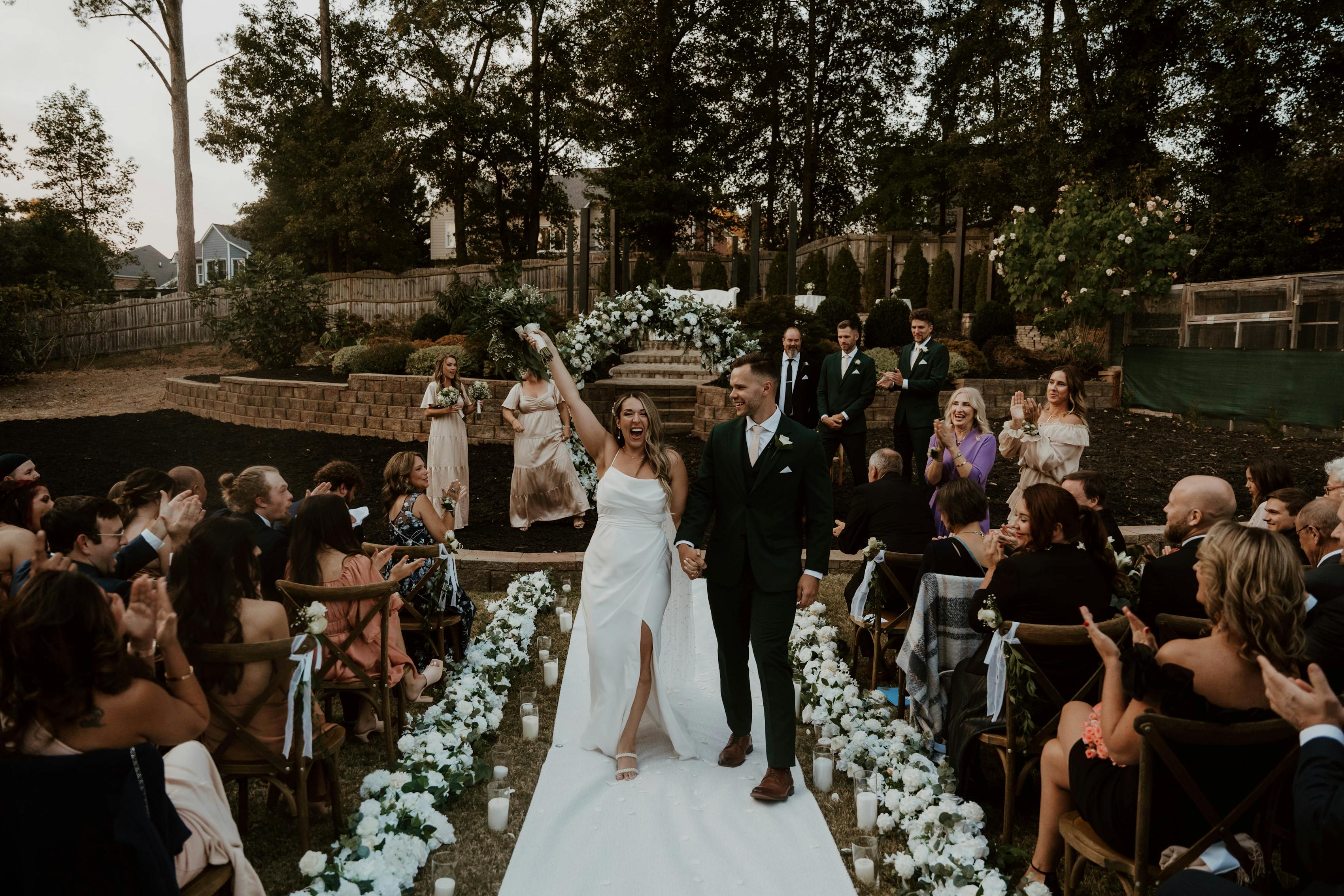 Walking through the white floral wedding arch and aisle.