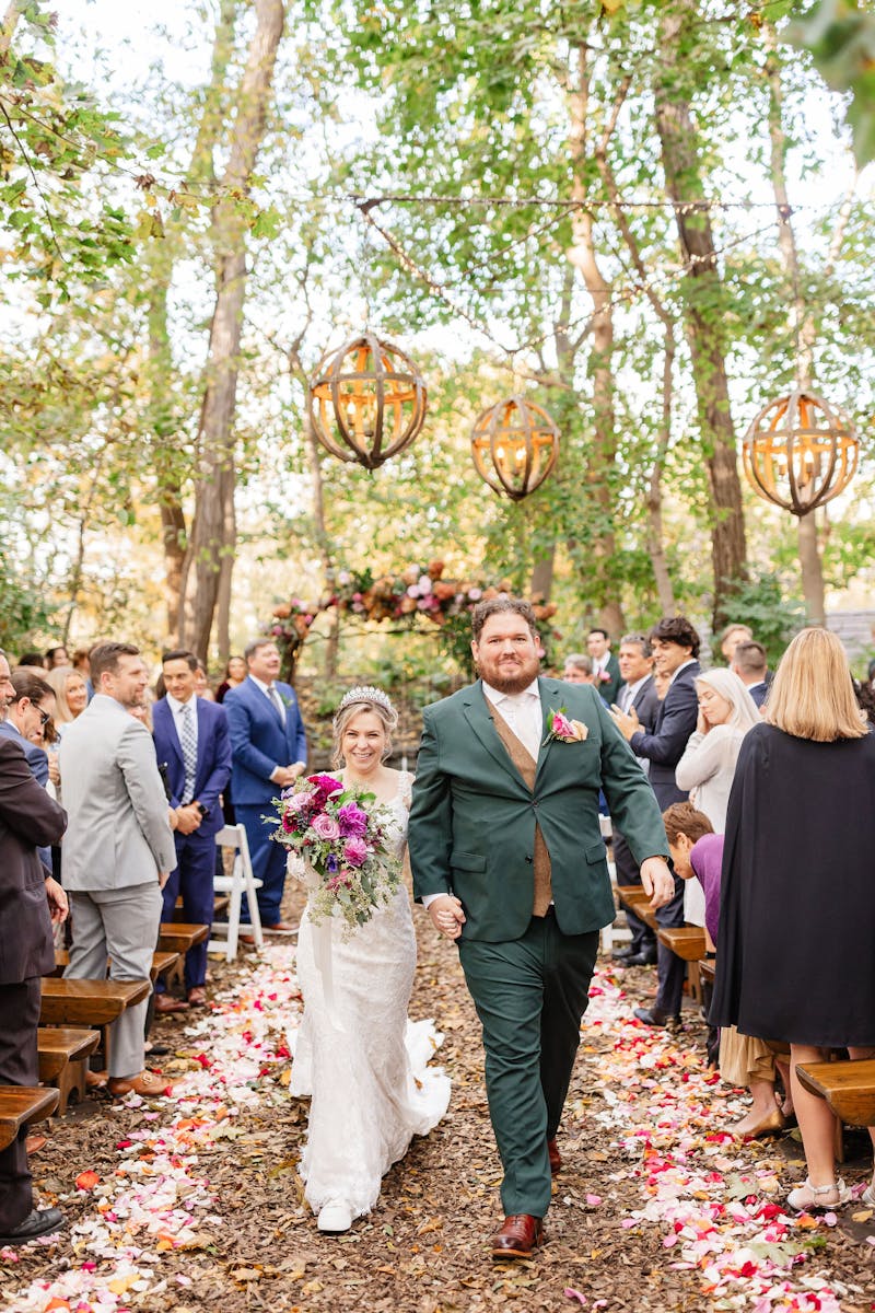 Fall bride in lace dress and groom in green suit and tweed vest at outdoor wedding ceremony.