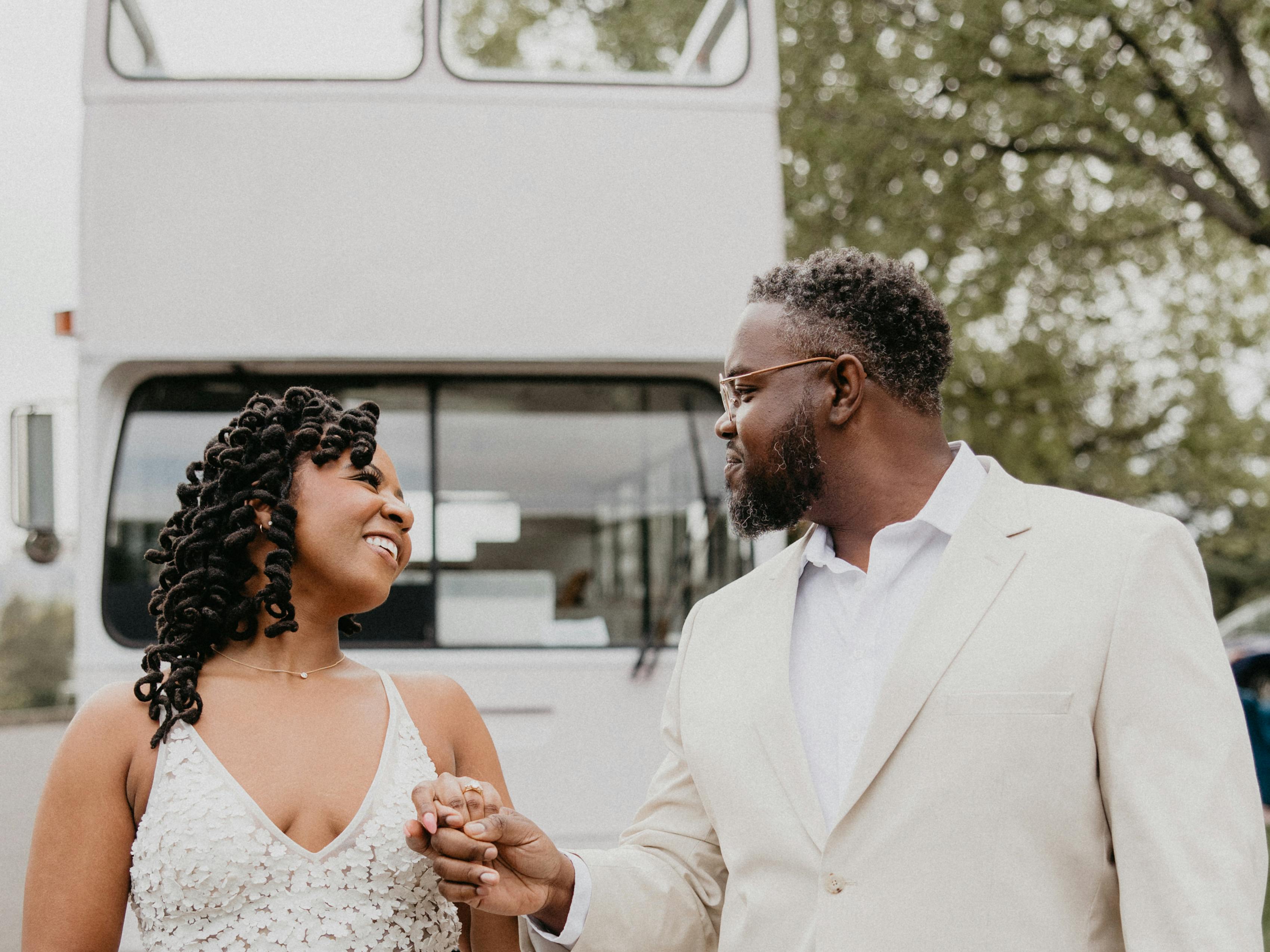 Modern style bride and groom holding hands in front of converted bus for unique wedding venue