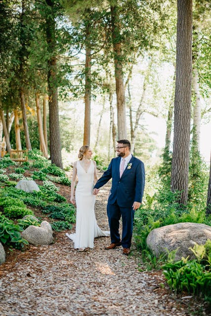 Bride and groom in Navy Suit surrounded by elegant greenery on their wedding day