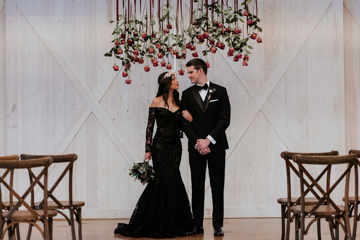 Edgy all-black wedding dress and black tuxedo with black bridal bouquet and hanging rose decoration wedding altar.