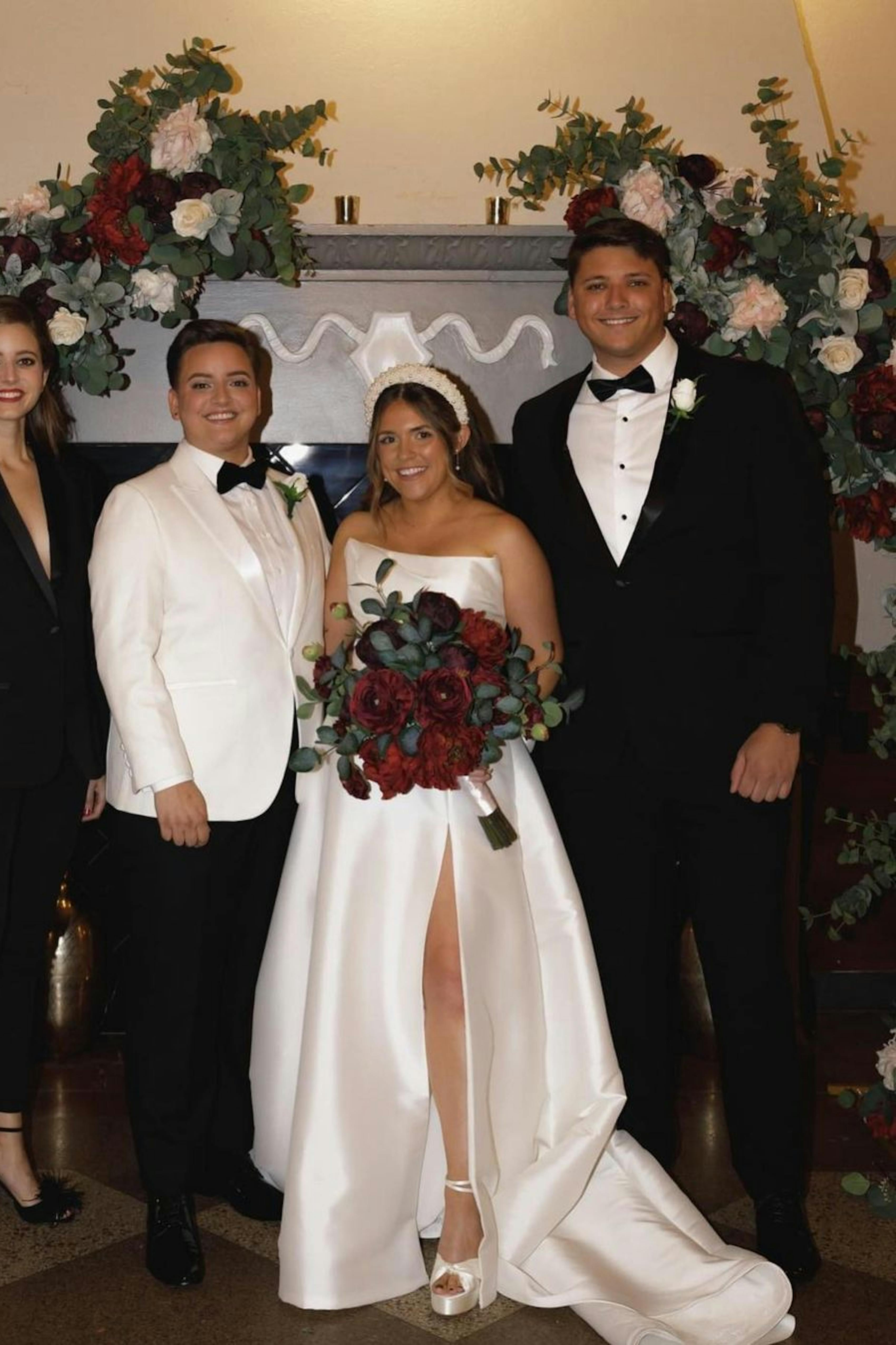 Mixed gender wedding party wearing a men's black tuxedo and a women's tuxedo around two brides wearing a a white wedding tuxedo for women and a white silk wedding ballgown