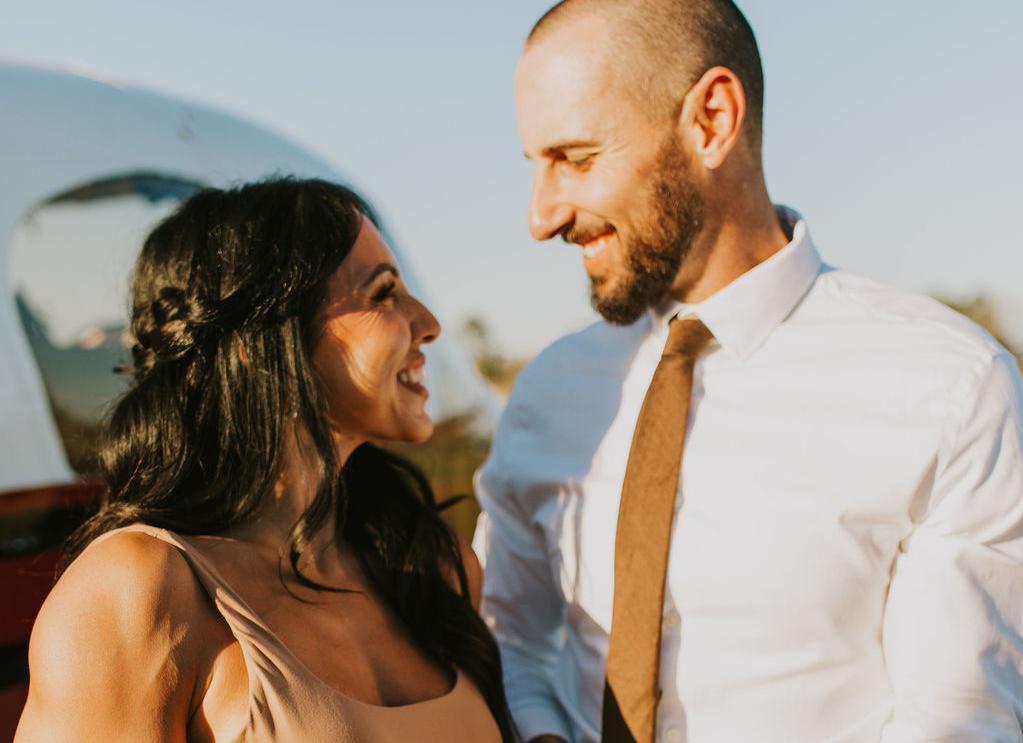 Couple wearing coordinated neutral outfits smiling at each other during a fall engagement photo session.