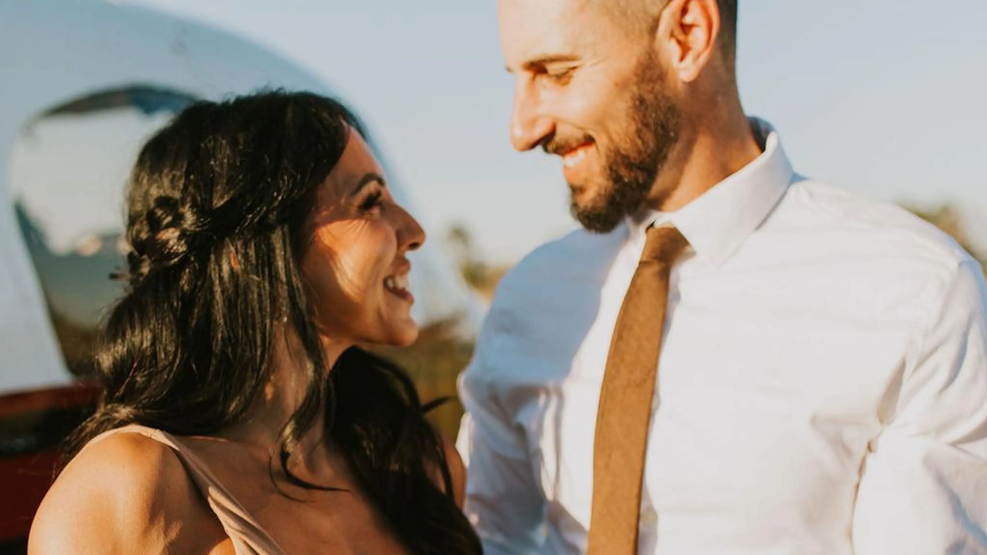 Couple wearing coordinated neutral outfits smiling at each other during a fall engagement photo session.