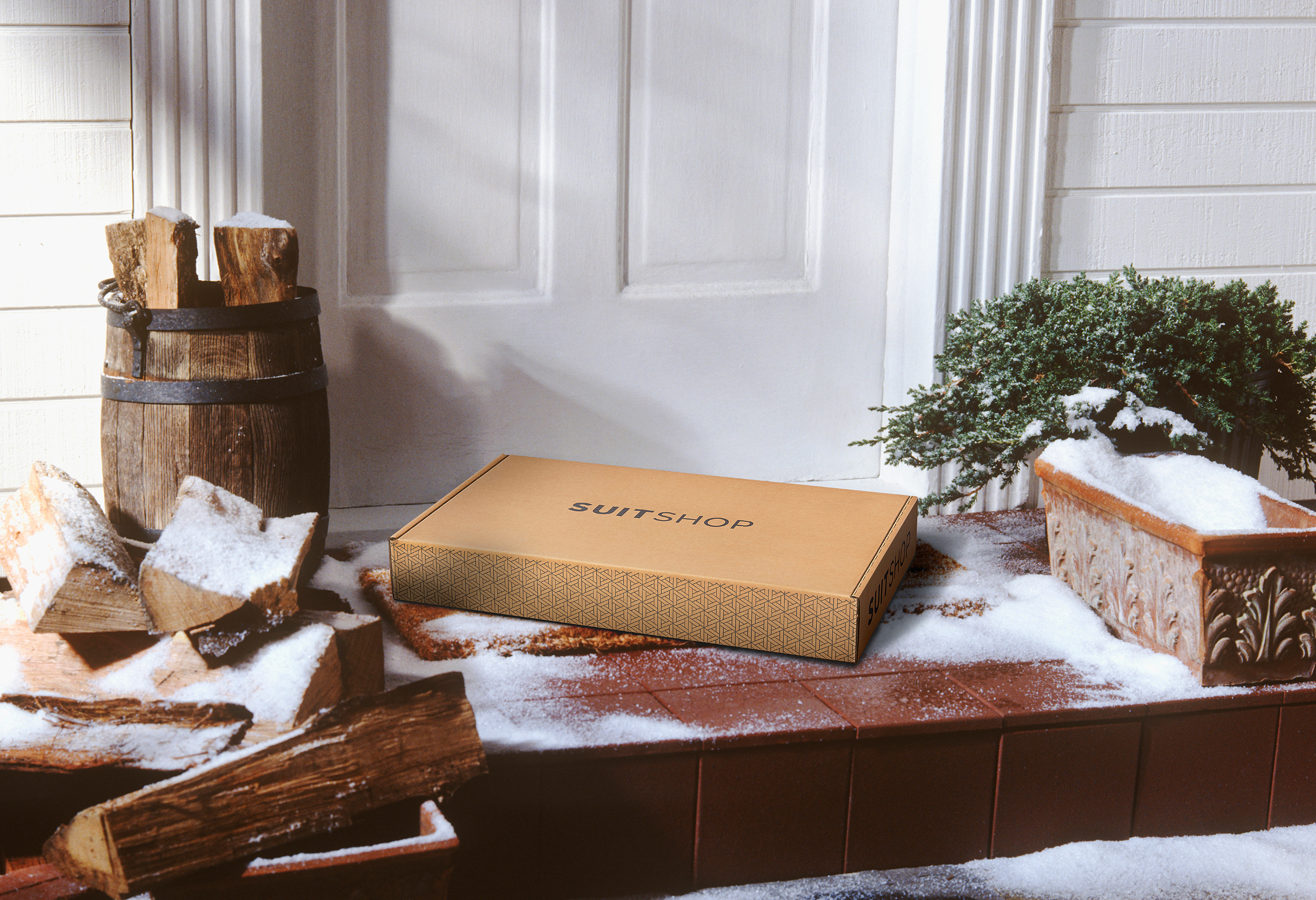 SuitShop delivery box on a snow-covered front porch beside stacked firewood and winter greenery.