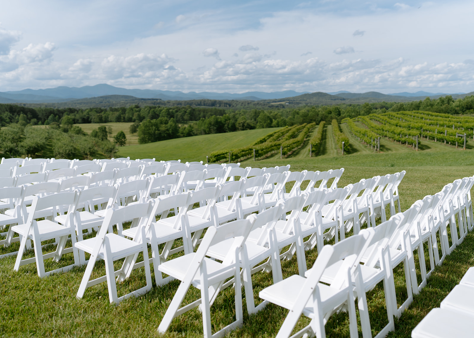 Outdoor vineyard wedding ceremony setup with rows of white chairs overlooking grapevines and mountain views
