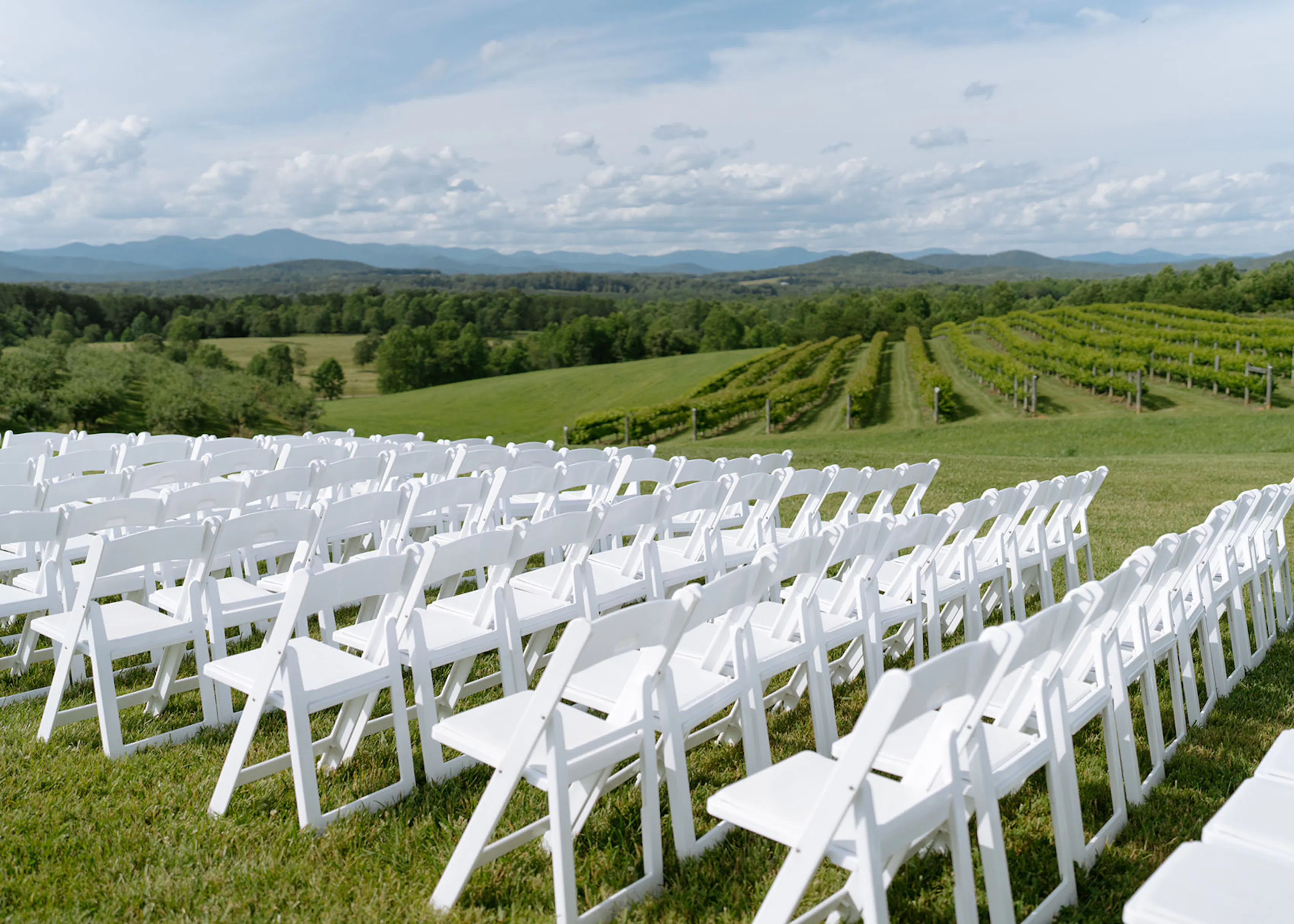 Outdoor vineyard wedding ceremony setup with rows of white chairs overlooking grapevines and mountain views