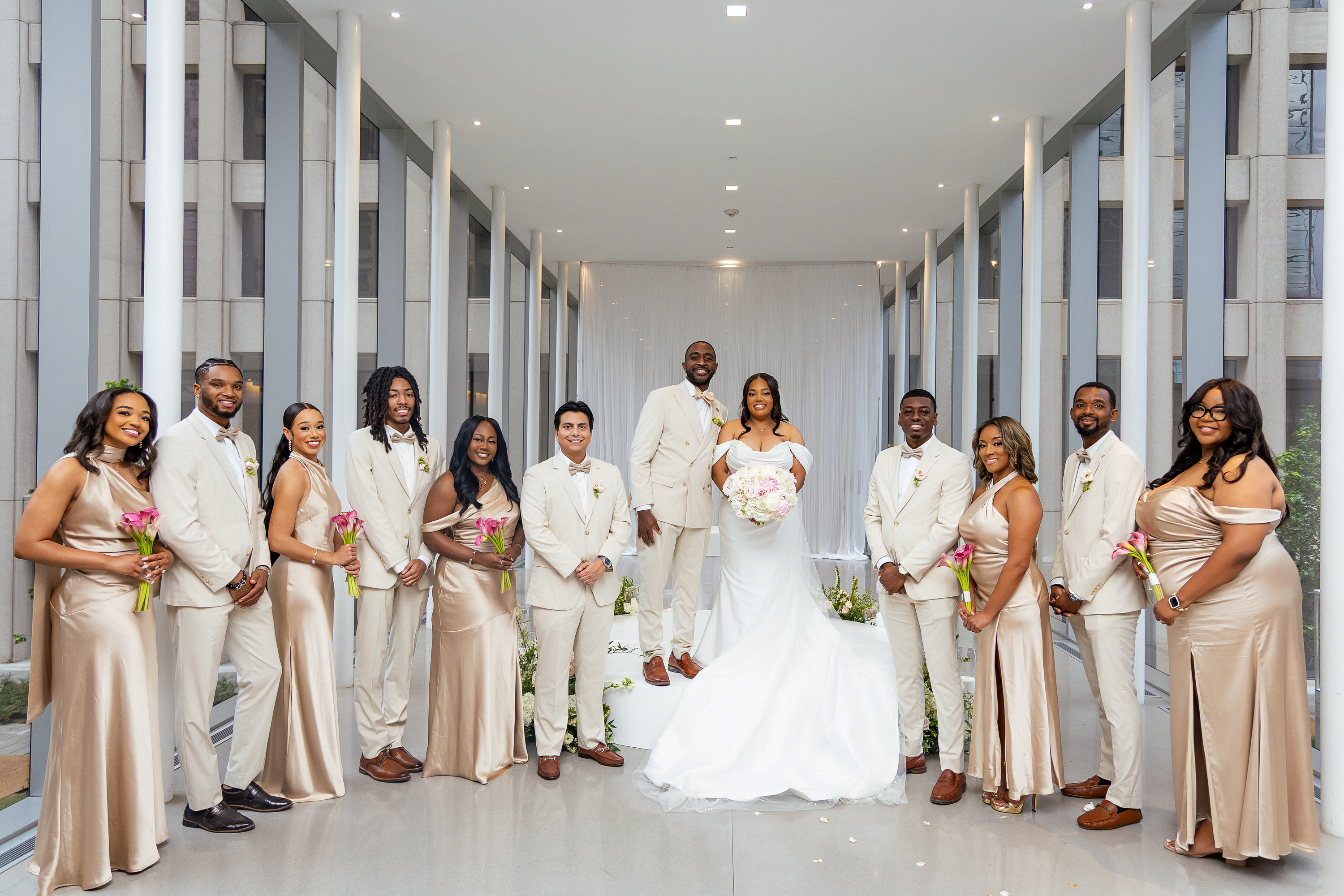 Wedding party wearing coordinated white groomsmen suits and champagne bridesmaid dresses for a modern wedding ceremony.