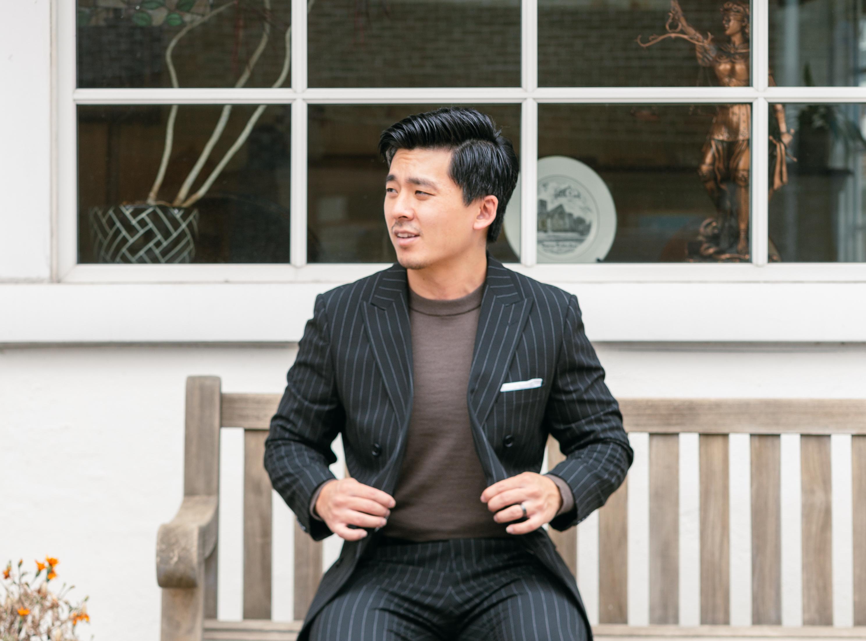 Man wearing a black pinstripe suit with a brown crewneck shirt for a casual wedding look.