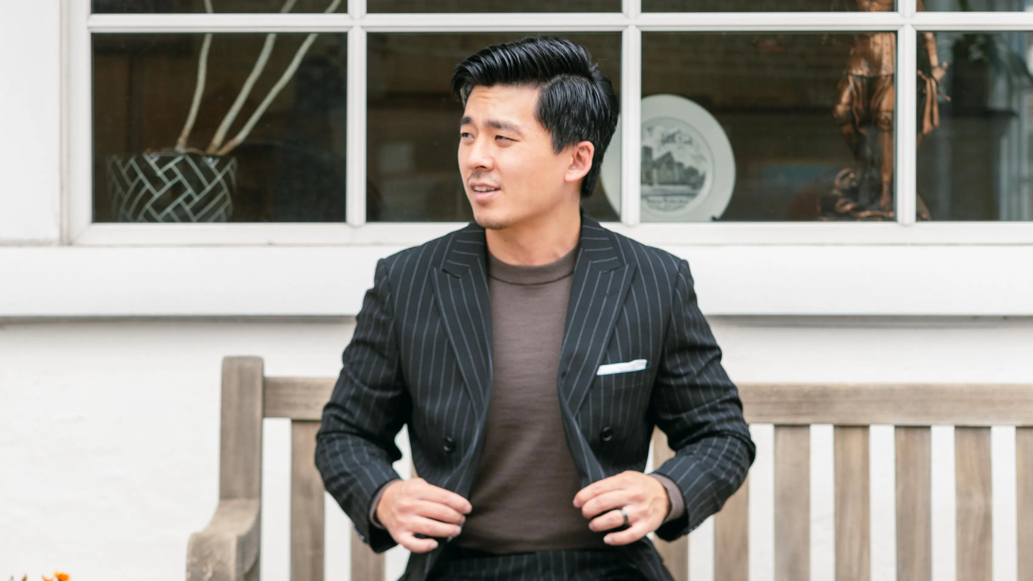 Man wearing a black pinstripe suit with a brown crewneck shirt for a casual wedding look.