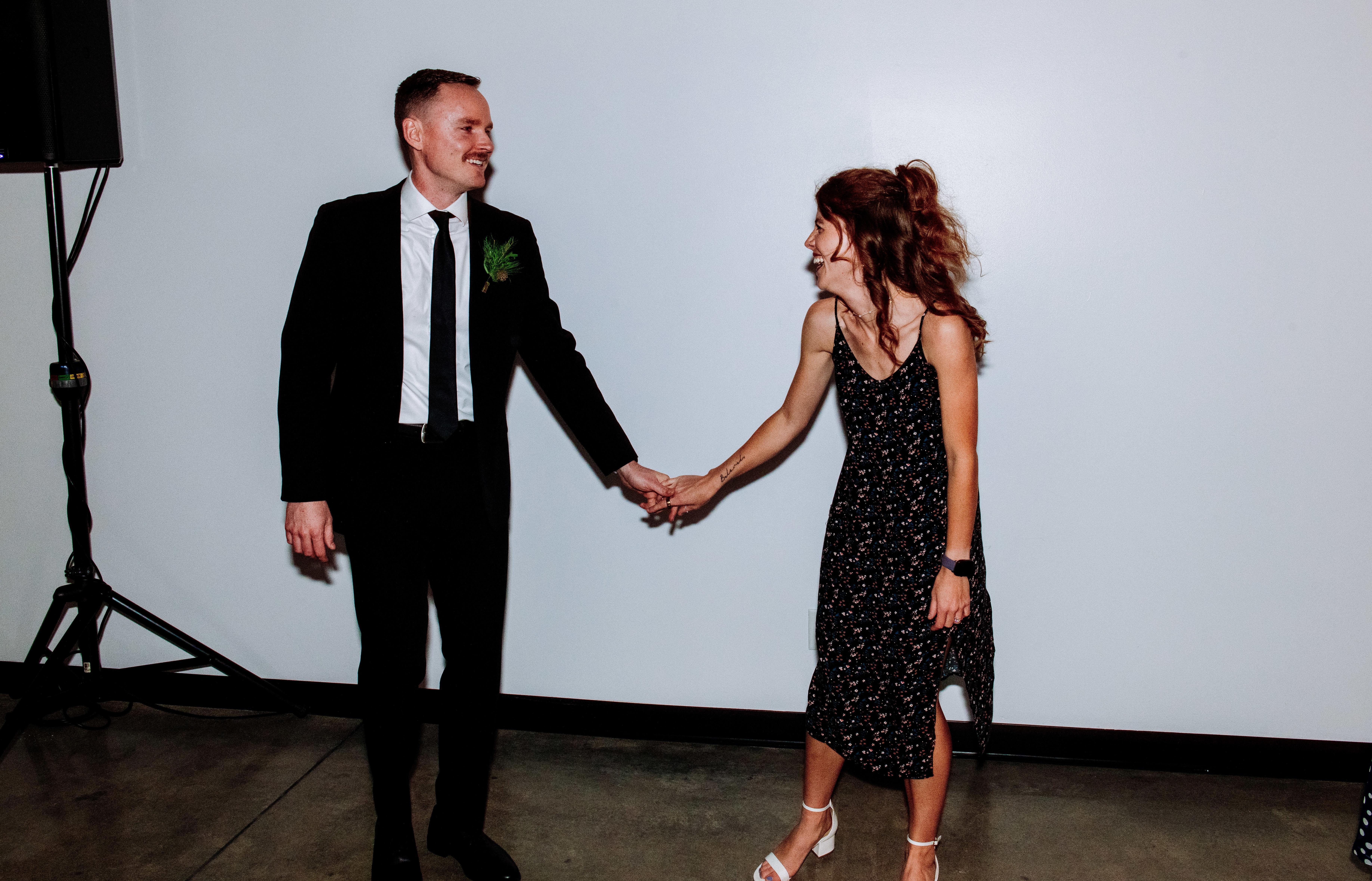 Wedding guests wearing black attire holding hands and smiling at a reception.