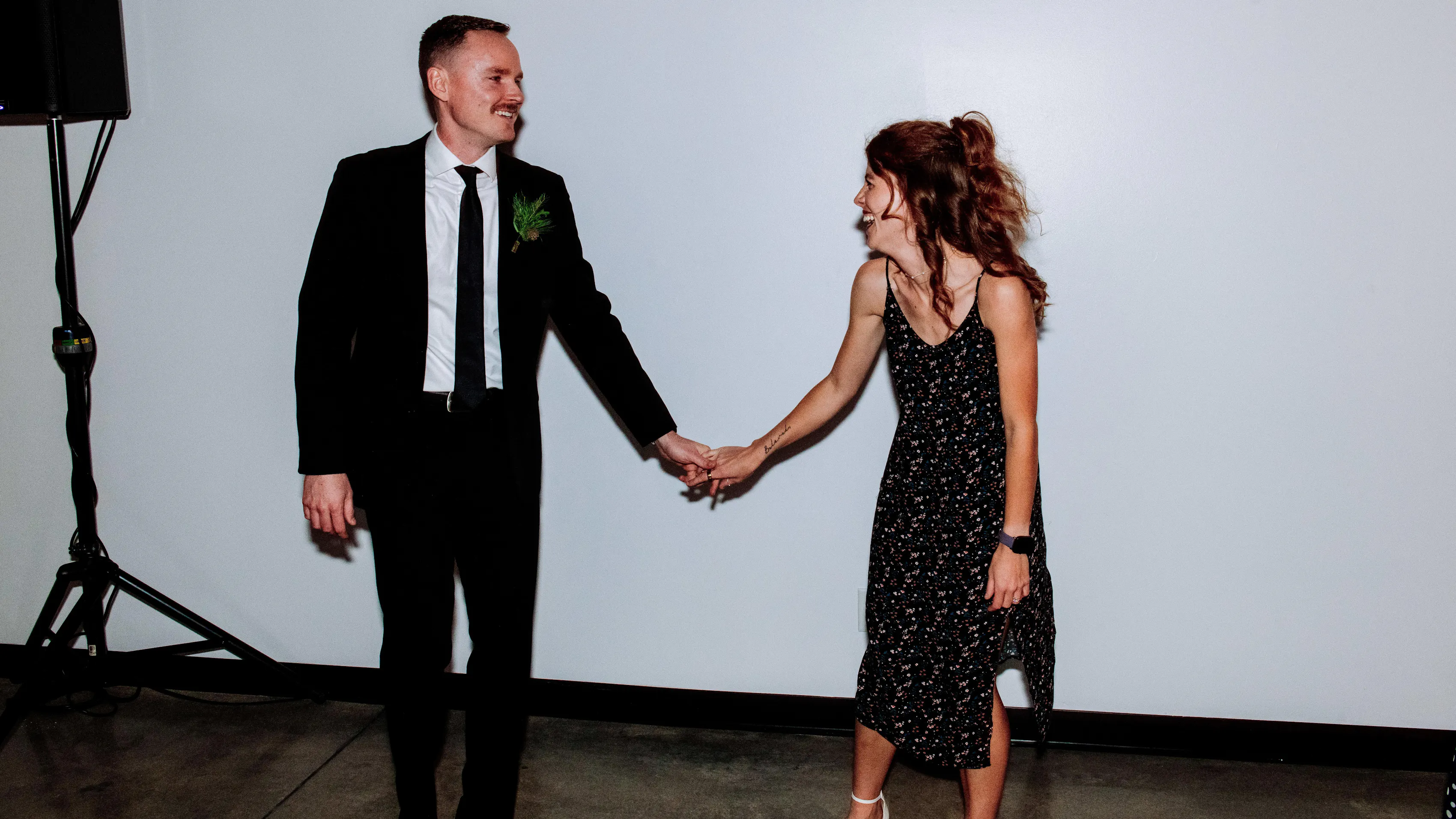 Wedding guests wearing black attire holding hands and smiling at a reception.