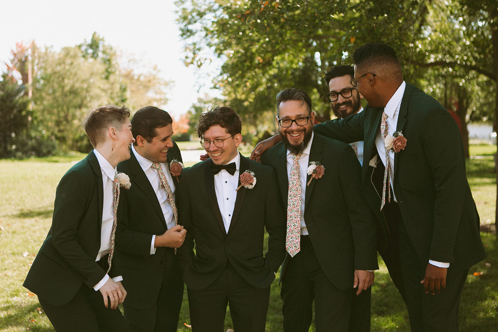 Wedding party wearing dark green suits with floral ties and fall-colored boutonnieres at an outdoor autumn wedding.