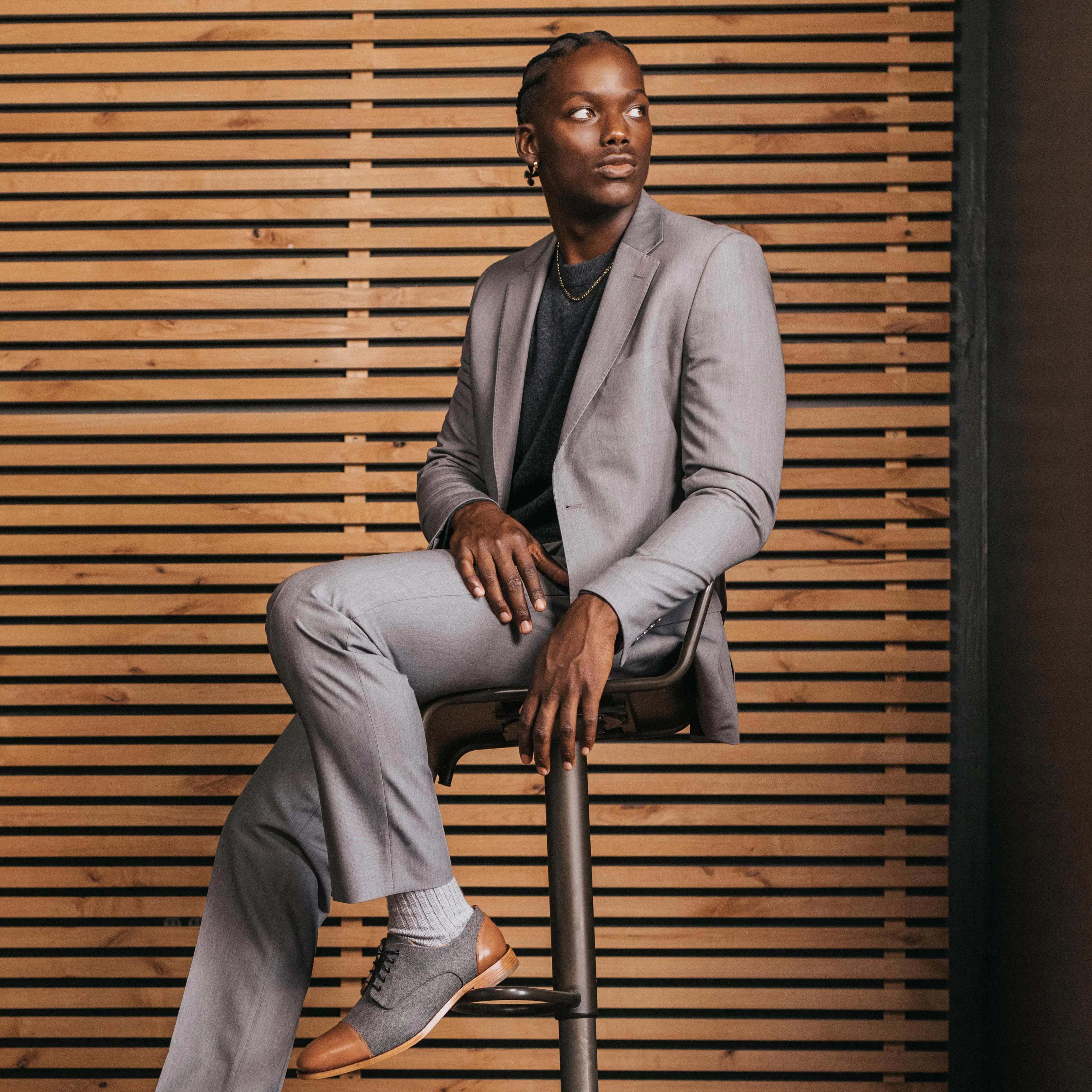 Man wearing a light gray suit with a dark crewneck shirt and two-tone dress shoes for a casual wedding look.