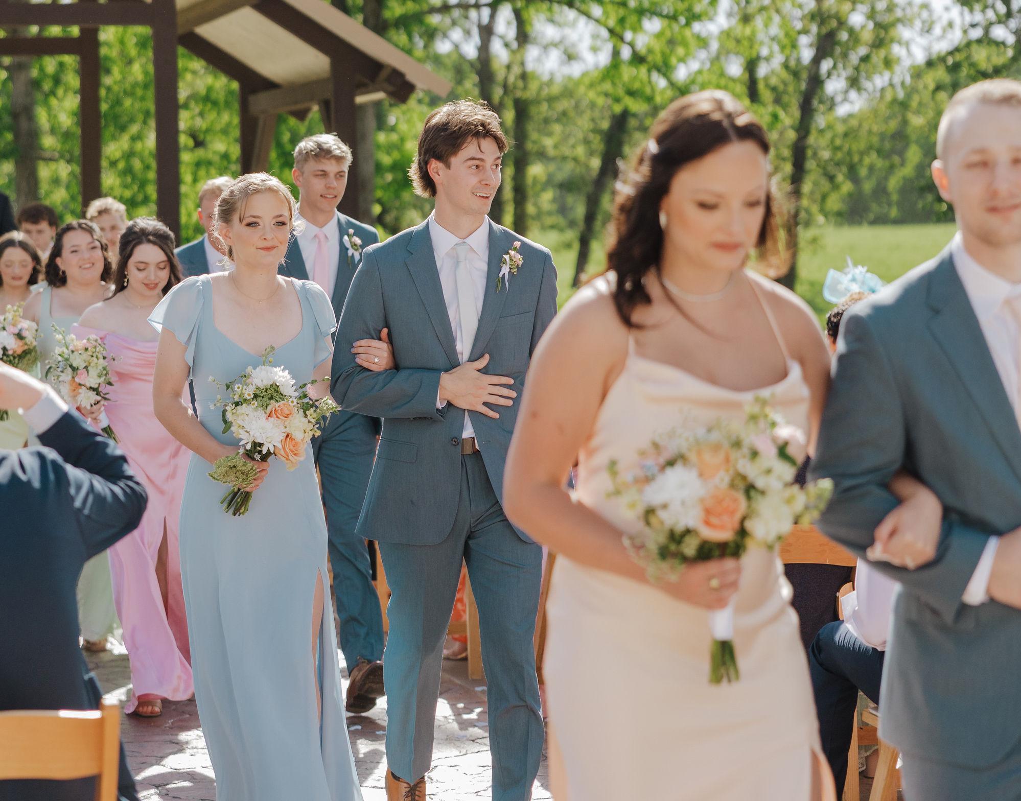 Wedding party wearing coordinated light blue suits and pastel dresses during an outdoor wedding ceremony.