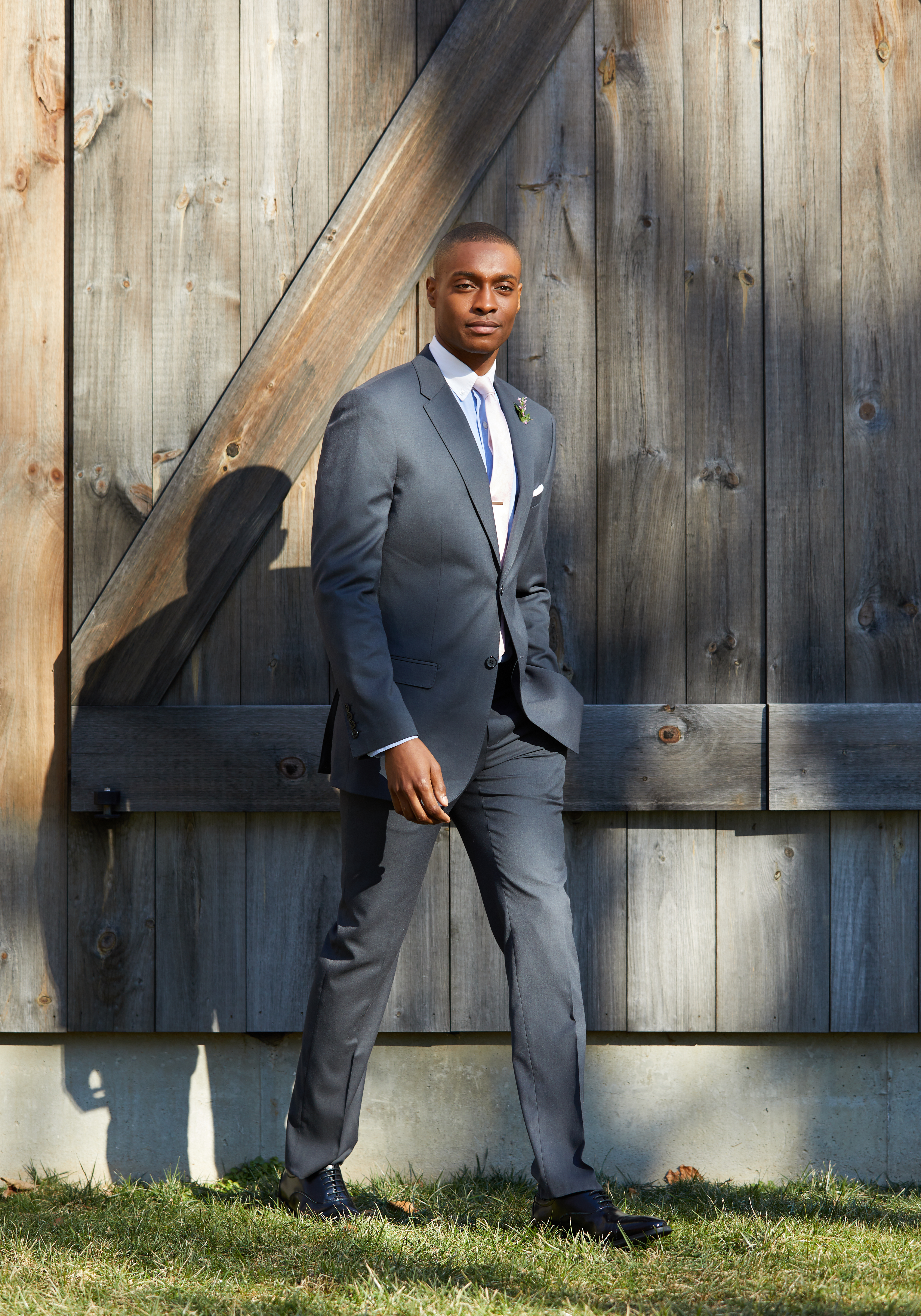 Man wearing a charcoal gray suit with a white dress shirt and light-colored tie at an outdoor fall wedding.