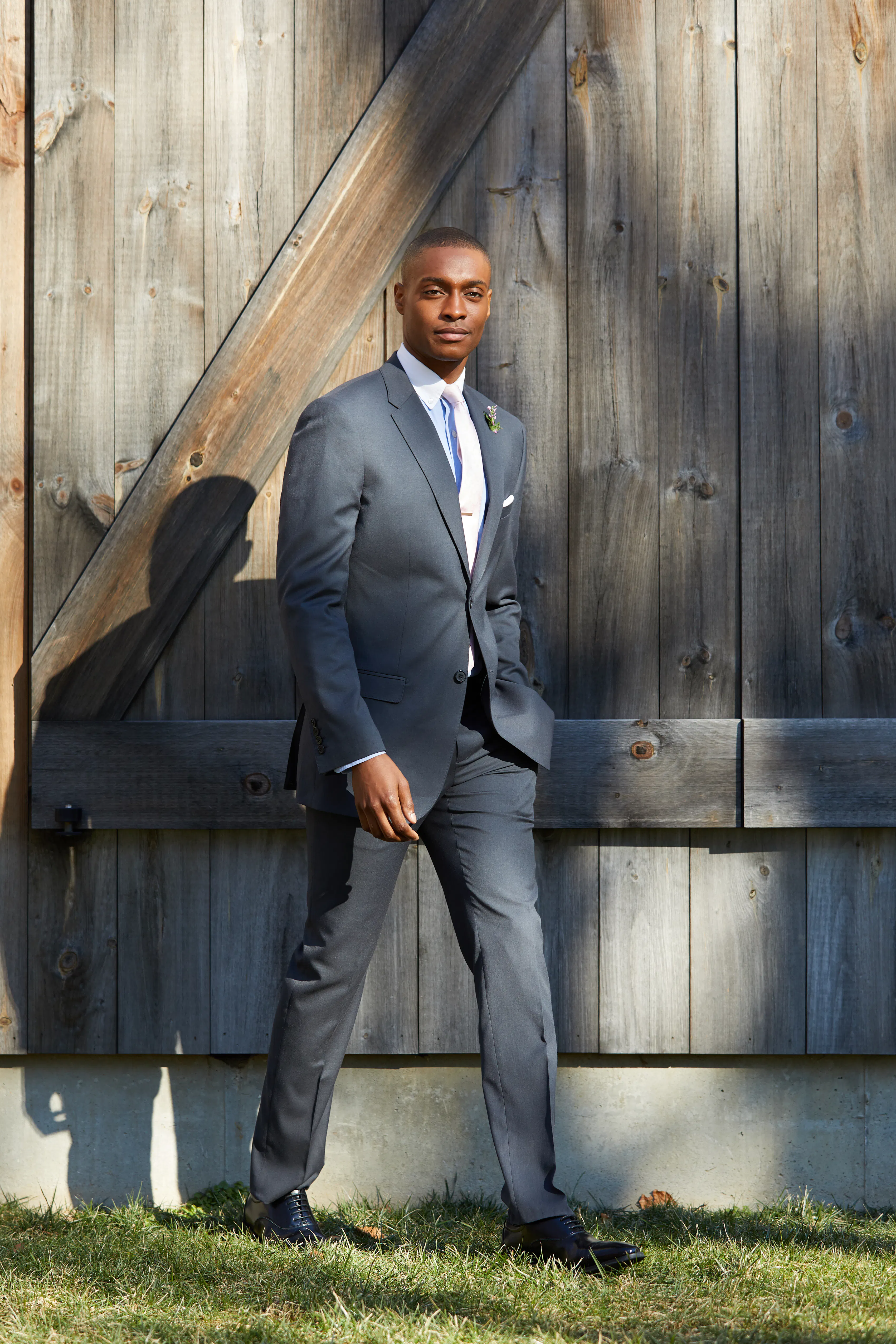 Man wearing a charcoal gray suit with a white dress shirt and light-colored tie at an outdoor fall wedding.