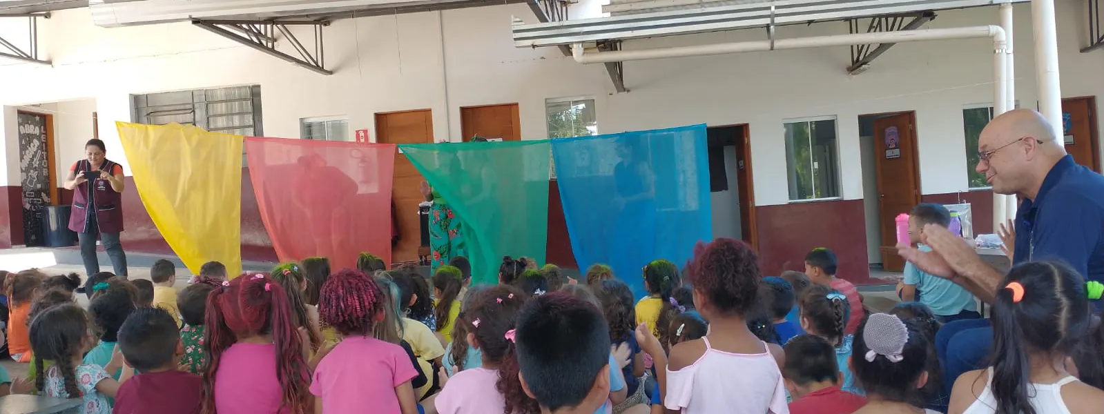 Na imagem mostra varias crianças da creche cei Sant Ana olhando para frente e batando palmas juntamente com a equipe da sulfoquimica e coordenadores da creche.