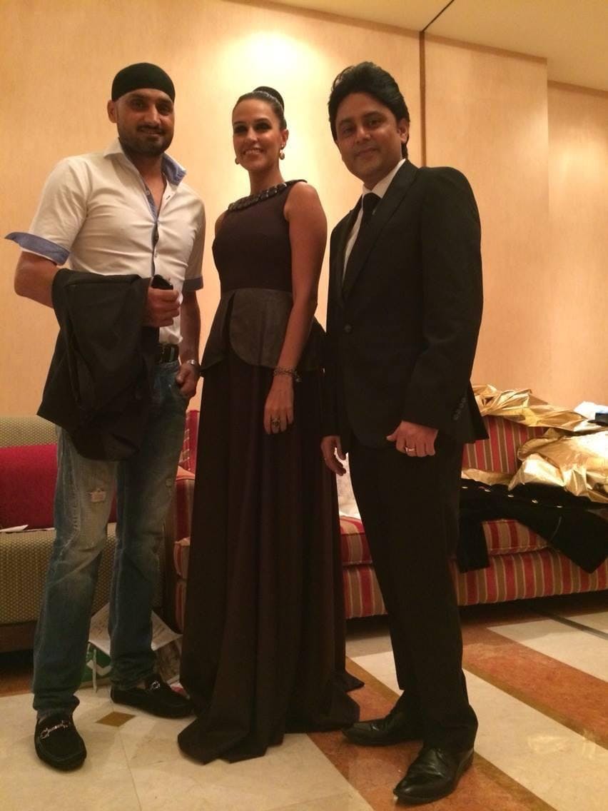 Harbhajan Singh in a white shirt and black turban standing next to Neha Dhupia in a dark gown and Dr. Sundeep Kochar in a black suit.