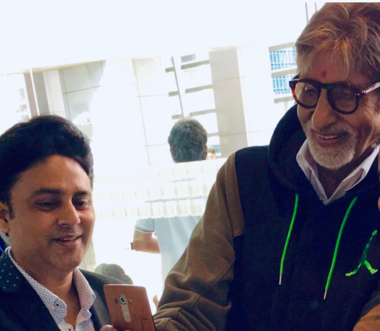 Amitabh Bachchan in a black Jordan hoodie and glasses looking at a phone alongside Dr. Sundeep Kochar.