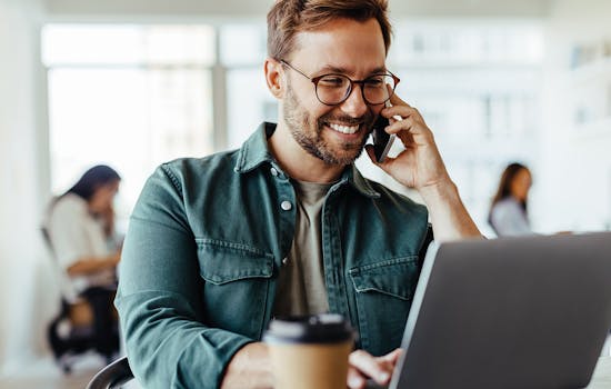 Man at an office with smart phone looking at laptop