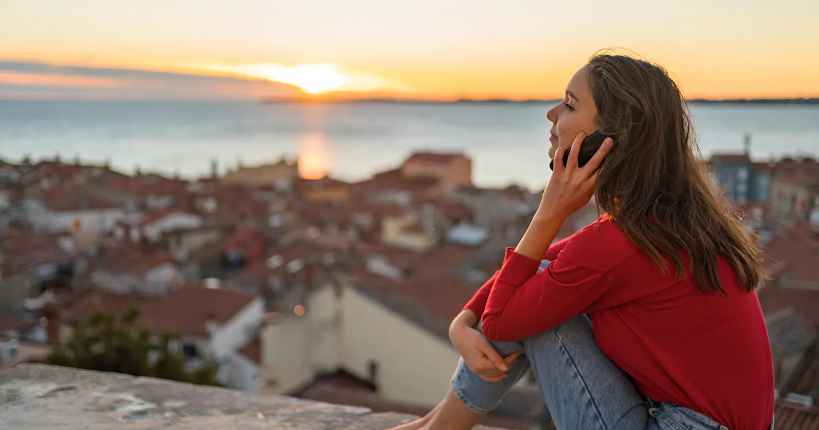 Woman making a phone call with sunset over the sea in the background