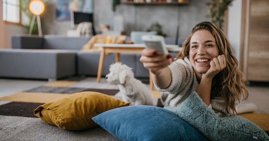 Woman lying on pillows in living room floor holding a TV remote control
