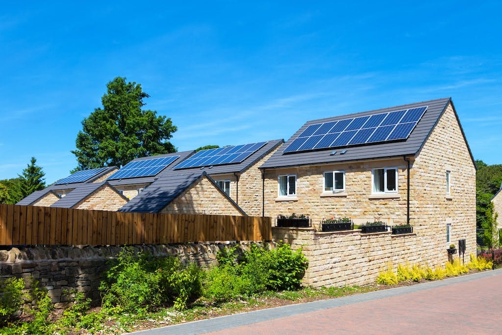 Solar panels on domestic rooftops in the UK, with blue sky and green trees
