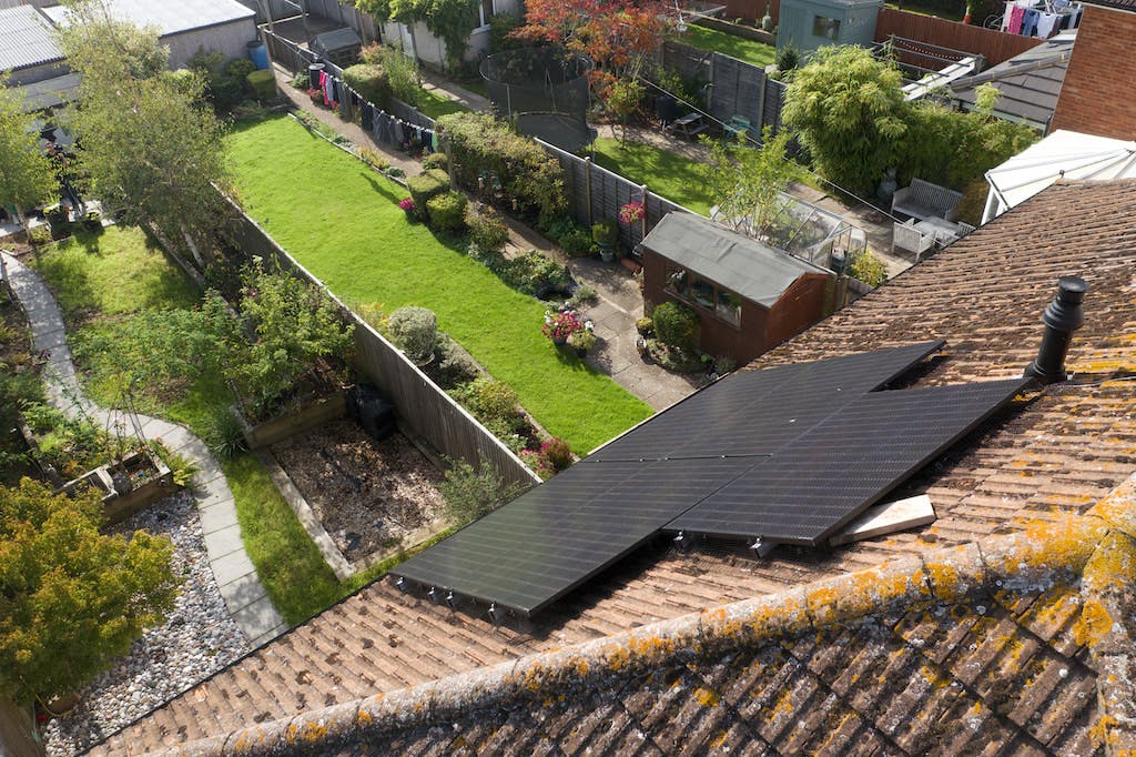 A black solar panel array on a UK rooftop as seen from above, looking down at a back garden