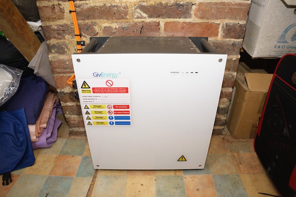 A white solar battery on the floor of a garage, against a bare brick wall