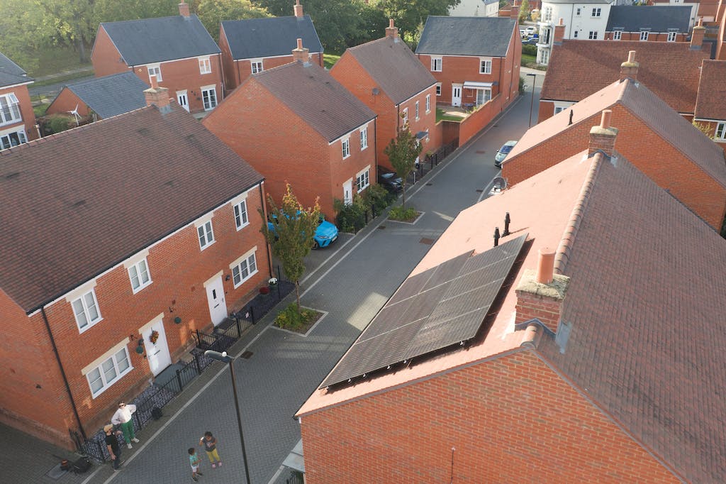 A black solar panel array on a house's rooftop, other red houses in the background