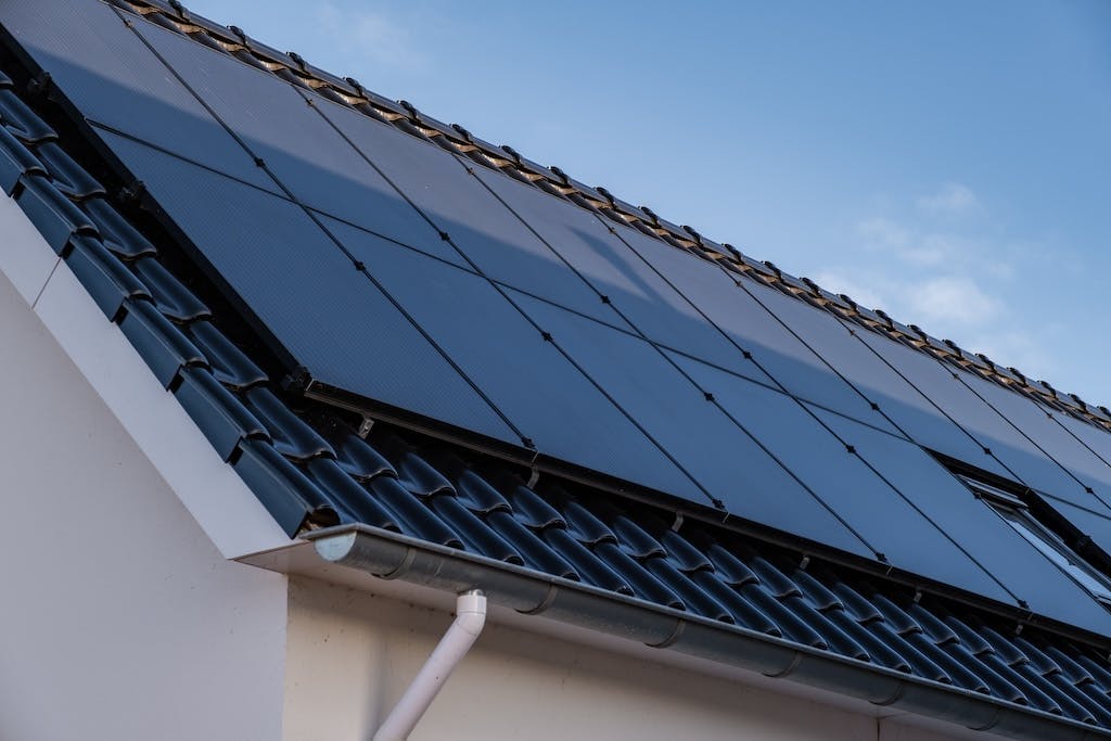 An array of black solar panels on a black-tiled roof, blue sky in the background