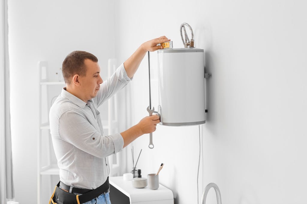 an engineer with a toolbelt measuring an electric boiler as he installs it