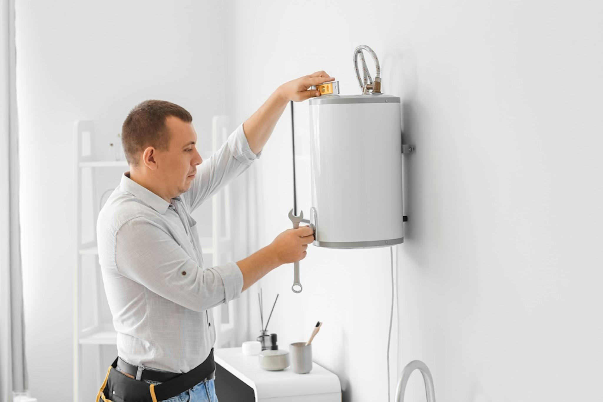 an engineer with a toolbelt measuring an electric boiler as he installs it