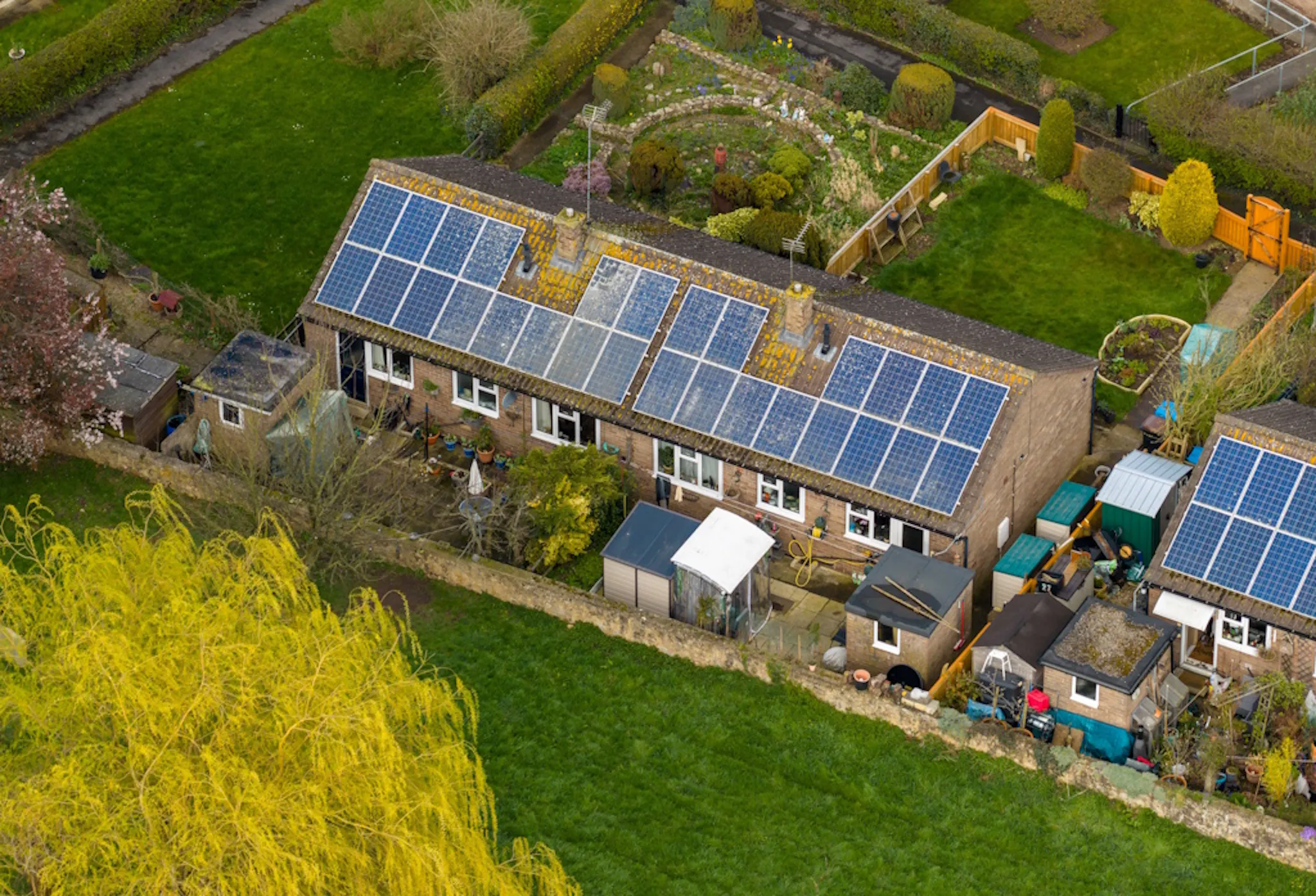 blue polycrystalline solar panels on a roof next to grass, greenery, and a neighbouring house
