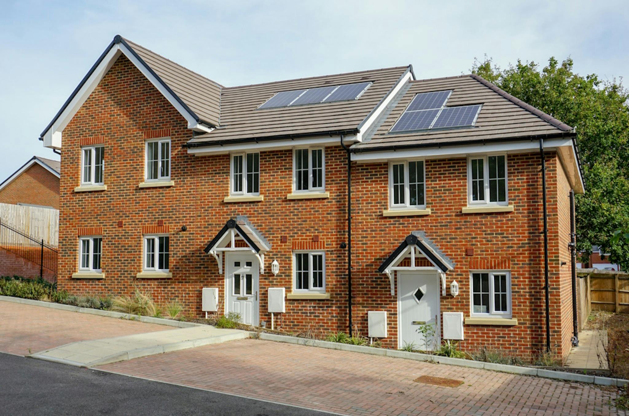 A brick house with solar panels on the roof, against a blue sky with some faint clouds