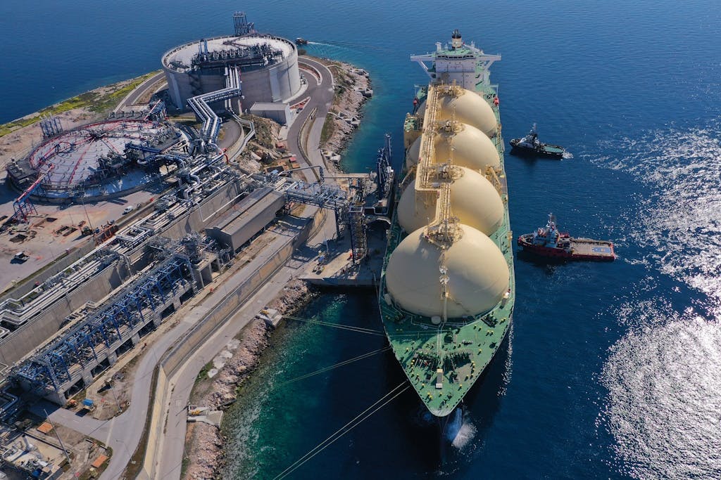 Aerial drone photo of an LNG (Liquified Natural Gas) tanker anchored on a sparkling blue sea next to the small LNG industrial islet of Revithoussa, in Greece, equipped with tanks for storage